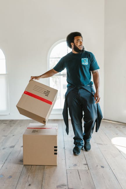 A person wearing a white T-shirt and blue jeans is packing a fragile item, specifically a large circular glass or ceramic plate, into a sturdy brown cardboard box. The person is holding the plate care